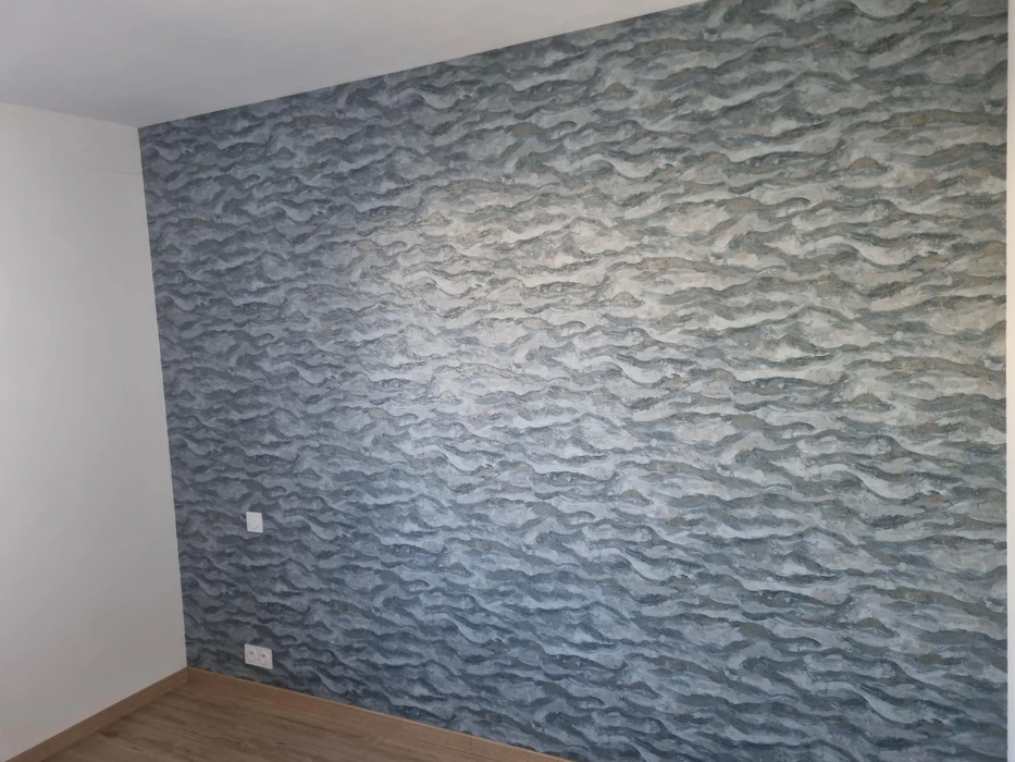 Intérieur résidentiel moderne avec mur d'accent décoratif. Une personne applique un revêtement texturé sur une surface murale blanche adjacente.