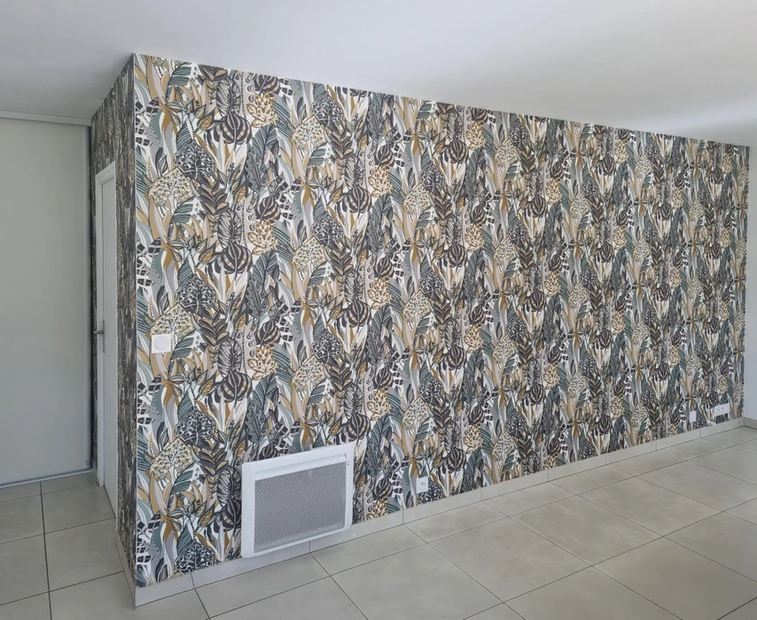 Intérieur résidentiel moderne avec mur entièrement recouvert de papier peint à motifs végétaux. Sol en carrelage beige clair, plinthes blanches, interrupteurs électriques visibles.