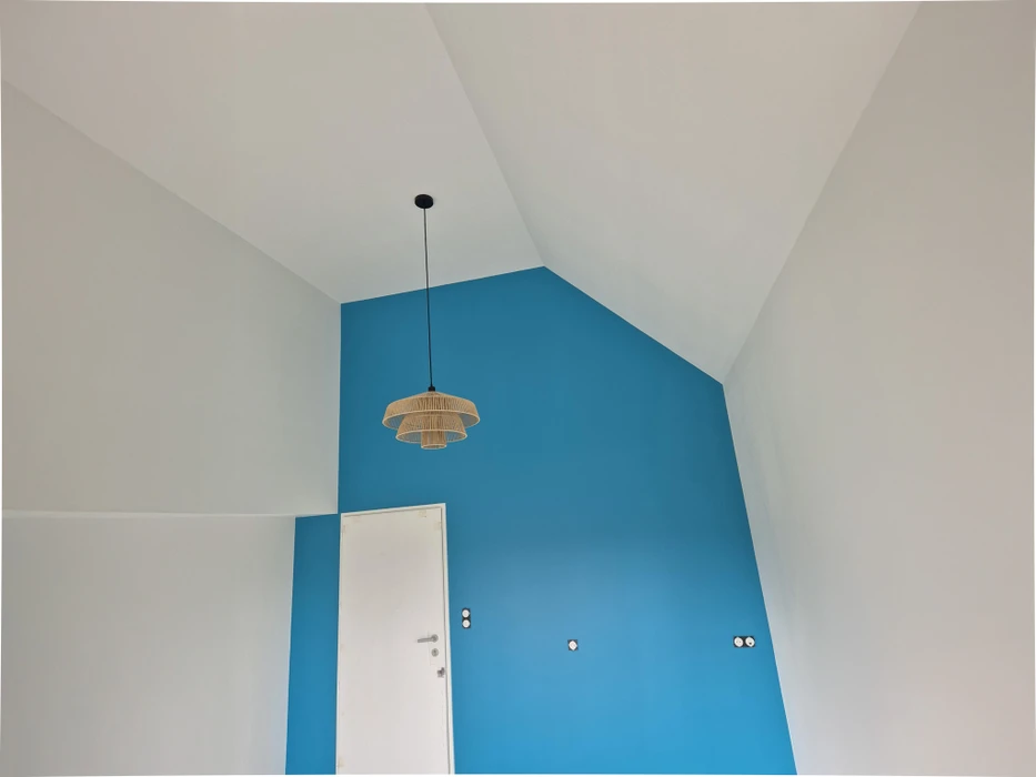 Chantier de rénovation intérieure en cours avec mur accent peint en terre cuite orange dans une pièce aux murs blancs. Prises électriques et interrupteurs noirs installés, câbles apparents en attente de finition. Sol protégé par bâche plastique.