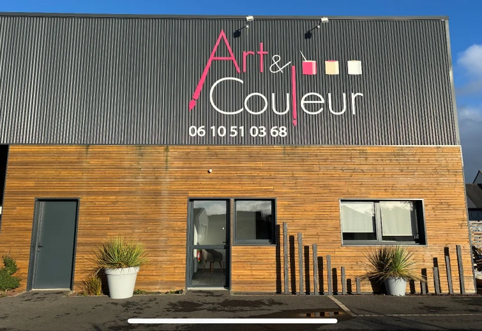 Homme en salopette et t-shirt blanc appliquant de la peinture blanche sur un mur intérieur avec un pinceau à manche rouge. Travaux de rénovation dans une pièce aux murs beiges avec plafond blanc et moulures décoratives.
