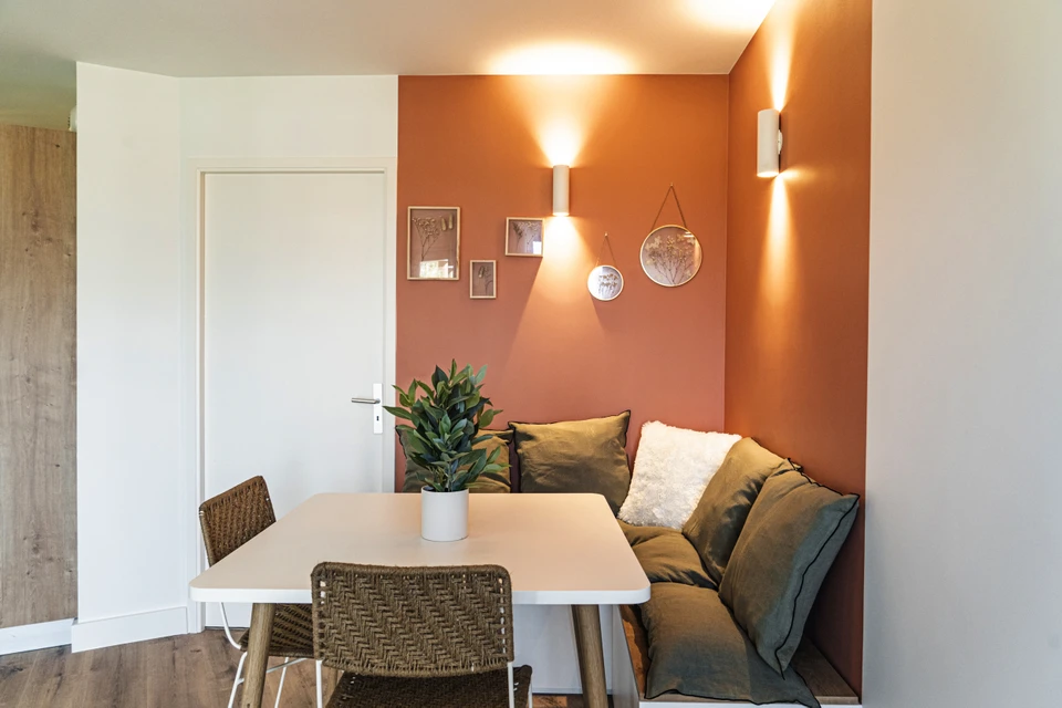 Chantier de rénovation intérieure avec deux échelles déployées dans une pièce aux murs blancs. Matériel de peinture au sol, seau jaune, bâches de protection. Plafonniers circulaires installés, menuiseries apparentes.