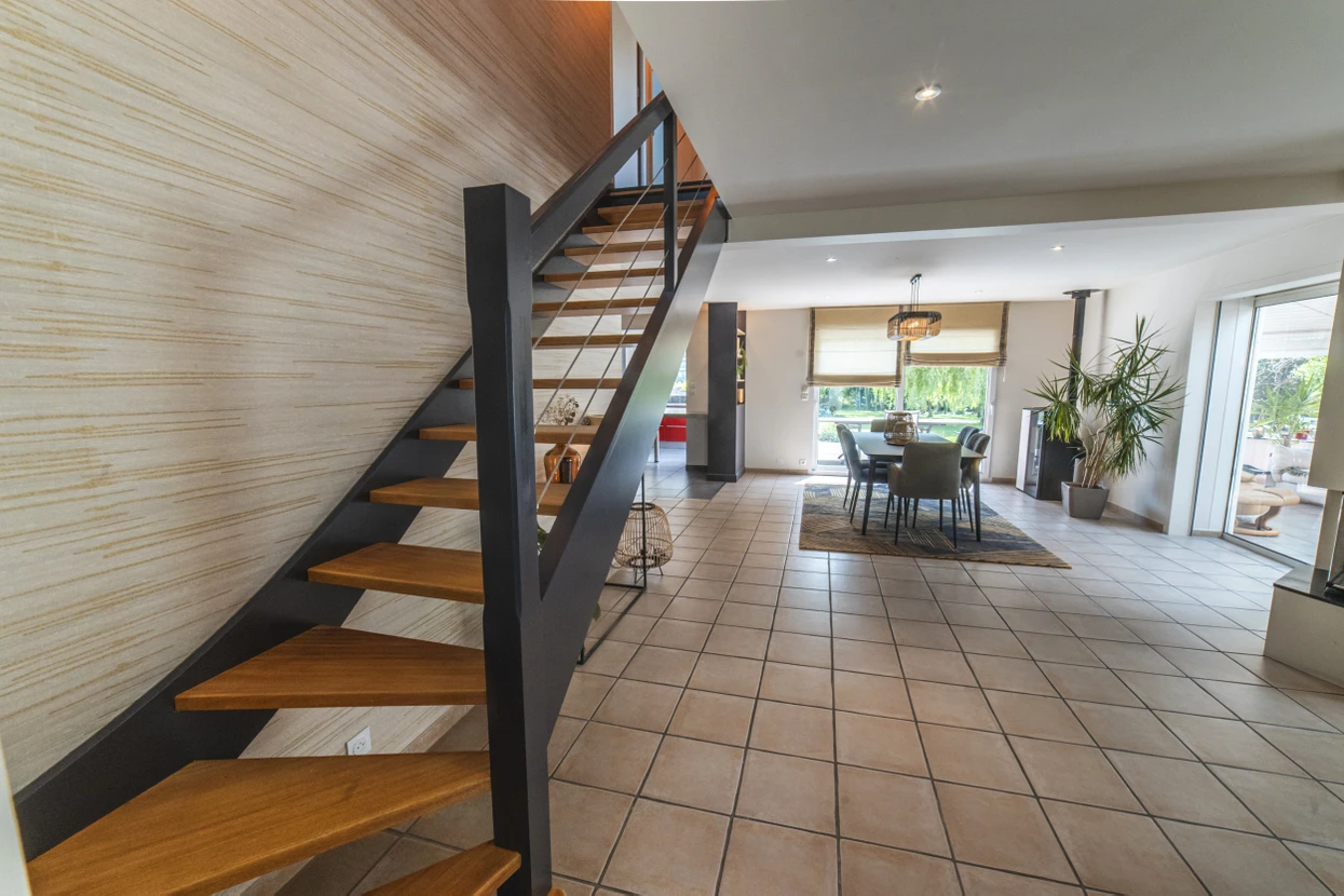 Mur intérieur en cours de peinture avec rouleau à peinture texturé. Main tenant un rouleau avec manche rouge appliquant une peinture beige sur surface murale blanche.