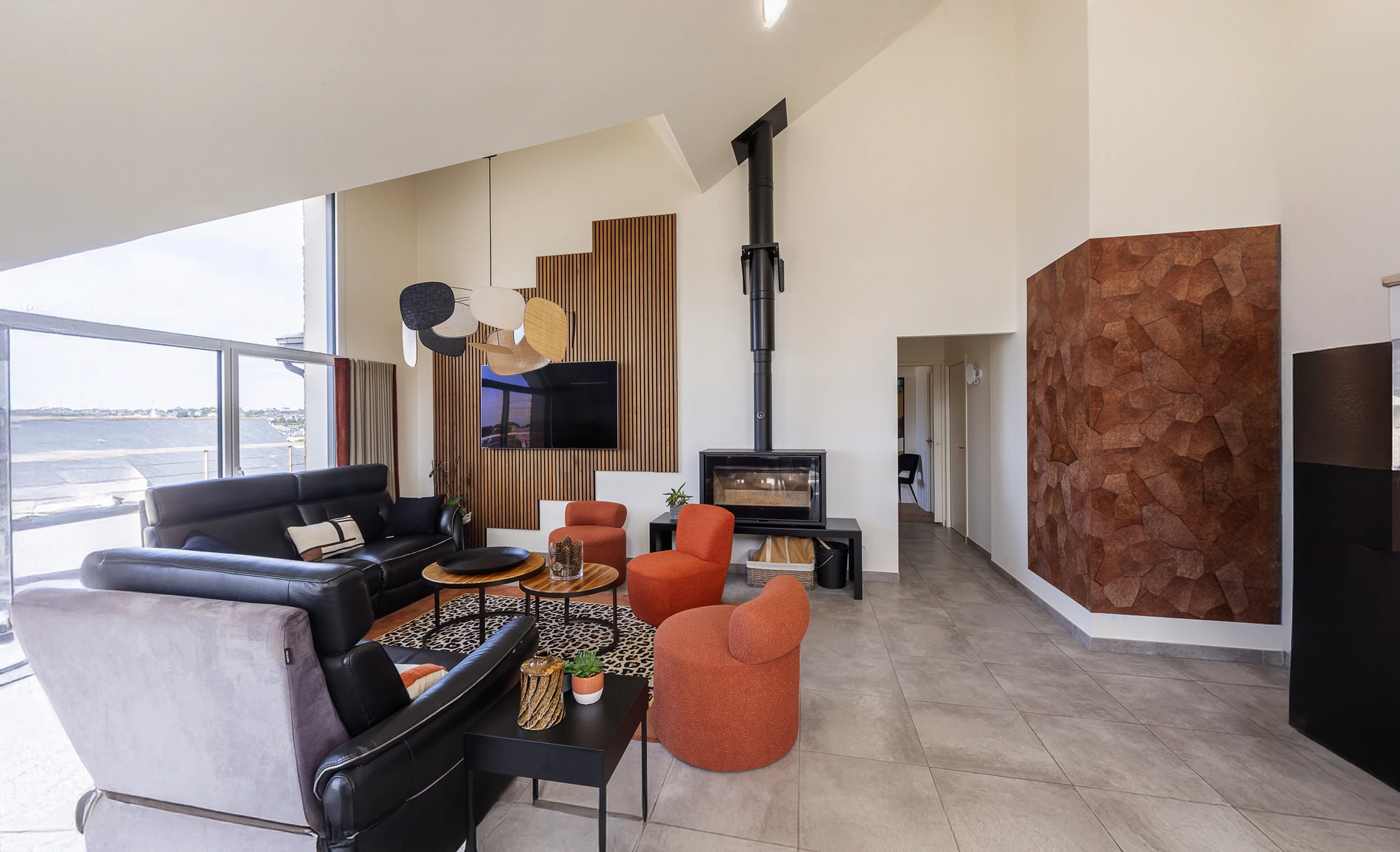 Extérieur d'une maison contemporaine blanche à étages avec bardage en ardoise grise sur pignon, fenêtres PVC blanches à volets roulants, toiture en tuiles sombres. Pelouse entretenue, clôture grillagée noire, ciel bleu nuageux.