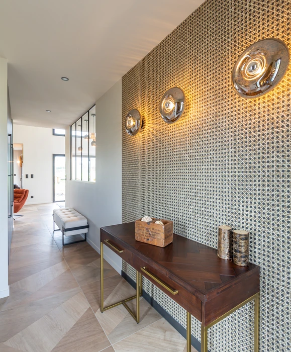 Intérieur résidentiel moderne avec mur d'accent orange terracotta contrastant avec murs blancs. Porte d'entrée sombre à gauche, grandes baies vitrées à cadre noir donnant sur l'extérieur à droite.