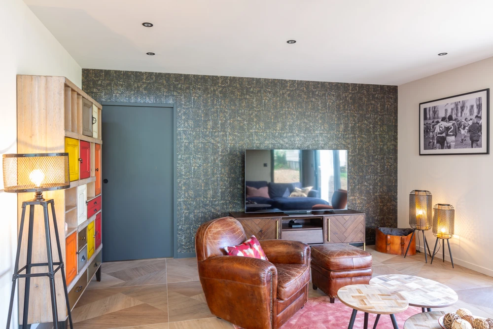 Chantier de rénovation intérieure en cours avec mur accent peint en terre cuite orange dans une pièce aux murs blancs. Prises électriques et interrupteurs noirs installés, câbles apparents en attente de finition. Sol protégé par bâche plastique.