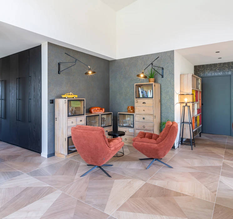 Chantier de rénovation intérieure en cours avec mur accent peint en terre cuite orange dans une pièce aux murs blancs. Prises électriques et interrupteurs noirs installés, câbles apparents en attente de finition. Sol protégé par bâche plastique.