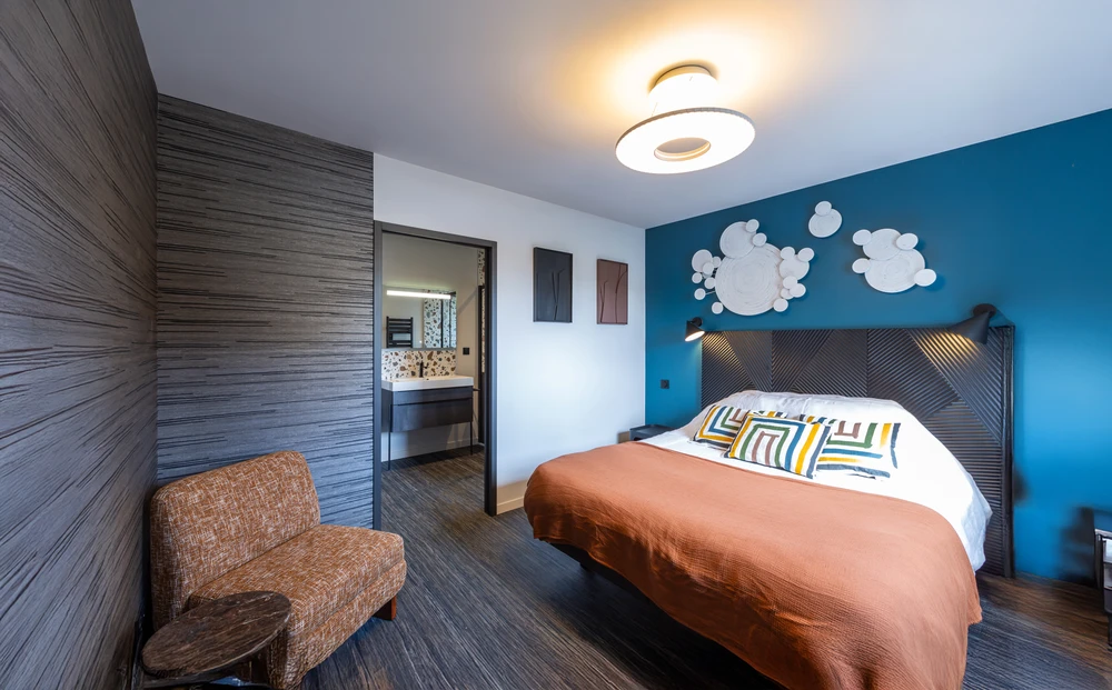 Femme peignant un mur intérieur en bleu turquoise avec rouleau à peinture dans appartement en cours d'aménagement. Cartons de déménagement empilés, plante décorative, fenêtres blanches avec cadres.