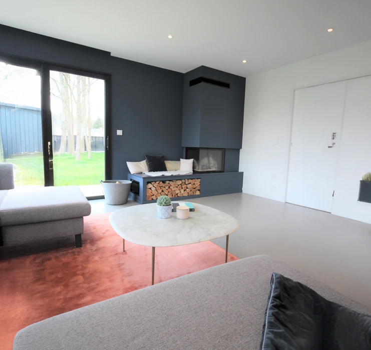 Intérieur résidentiel moderne avec mur d'accent orange terracotta contrastant avec murs blancs. Porte d'entrée sombre à gauche, grandes baies vitrées à cadre noir donnant sur l'extérieur à droite.