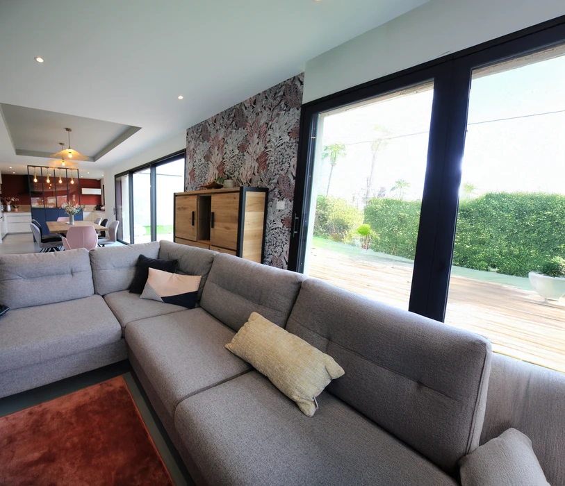 Chantier de rénovation intérieure en cours avec mur accent peint en terre cuite orange dans une pièce aux murs blancs. Prises électriques et interrupteurs noirs installés, câbles apparents en attente de finition. Sol protégé par bâche plastique.