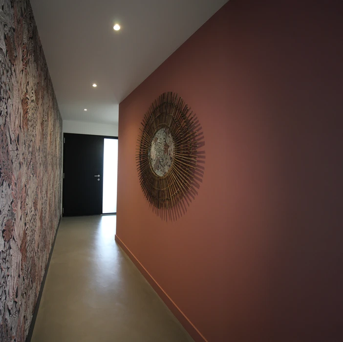 Intérieur d'une pièce en cours de finition avec mur accent peint en ocre jaune. Une personne travaille sur les finitions murales. Fenêtre avec encadrement noir sur mur blanc latéral.