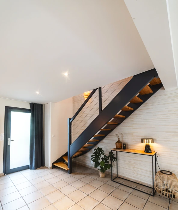 Chantier de rénovation intérieure en cours avec mur accent peint en terre cuite orange dans une pièce aux murs blancs. Prises électriques et interrupteurs noirs installés, câbles apparents en attente de finition. Sol protégé par bâche plastique.