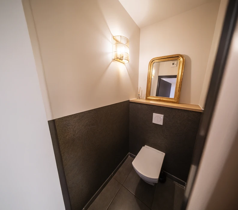 Intérieur d'atelier avec pistolet à peinture rouge au premier plan. L'outil de pulvérisation professionnelle comprend un réservoir métallique chromé à alimentation par gravité, une gâchette ergonomique, un raccord pneumatique fileté et une buse de projection réglable. Équipement de peinture industrielle pour application de revêtements.