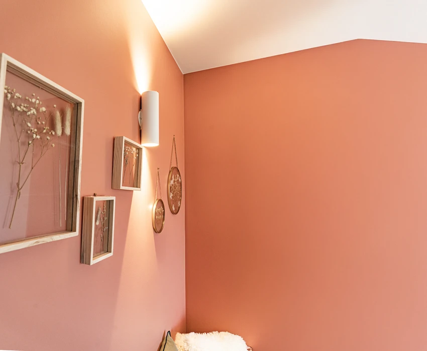 Intérieur résidentiel moderne avec mur d'accent orange terracotta contrastant avec murs blancs. Porte d'entrée sombre à gauche, grandes baies vitrées à cadre noir donnant sur l'extérieur à droite.
