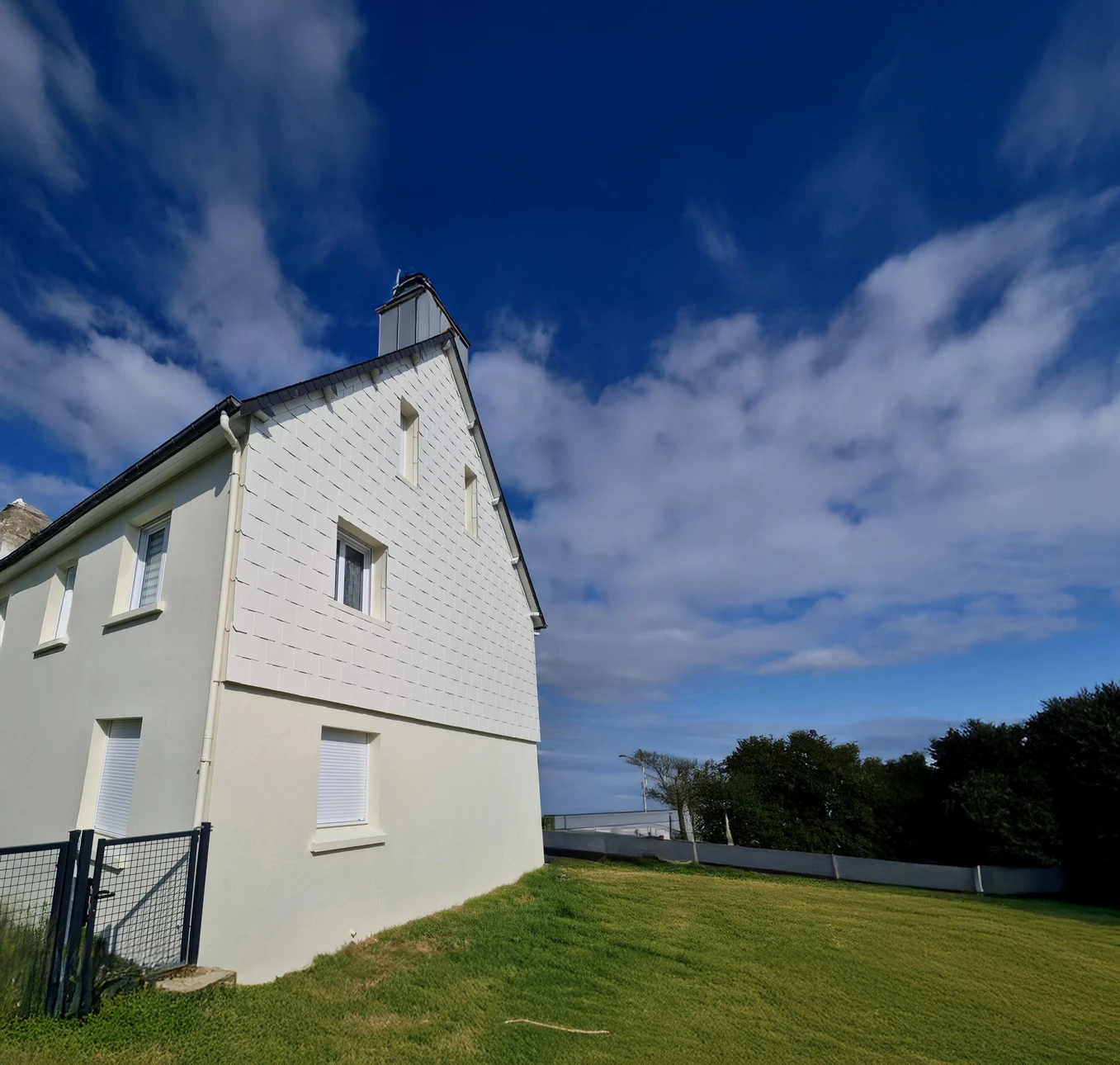 Maison contemporaine à étage avec façade jaune claire et toiture grise à tuiles, située dans un environnement paysager soigné