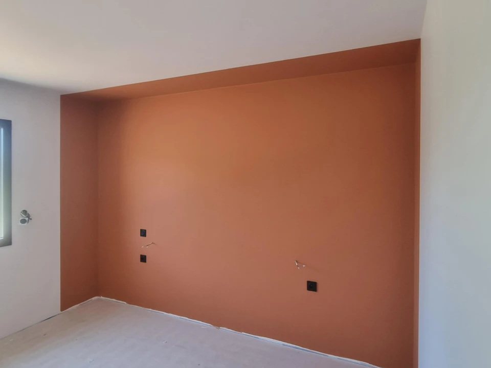 Atelier de peinture automobile professionnel avec technicien en combinaison intégrale blanche appliquant la peinture au pistolet sur carrosserie de véhicule sombre